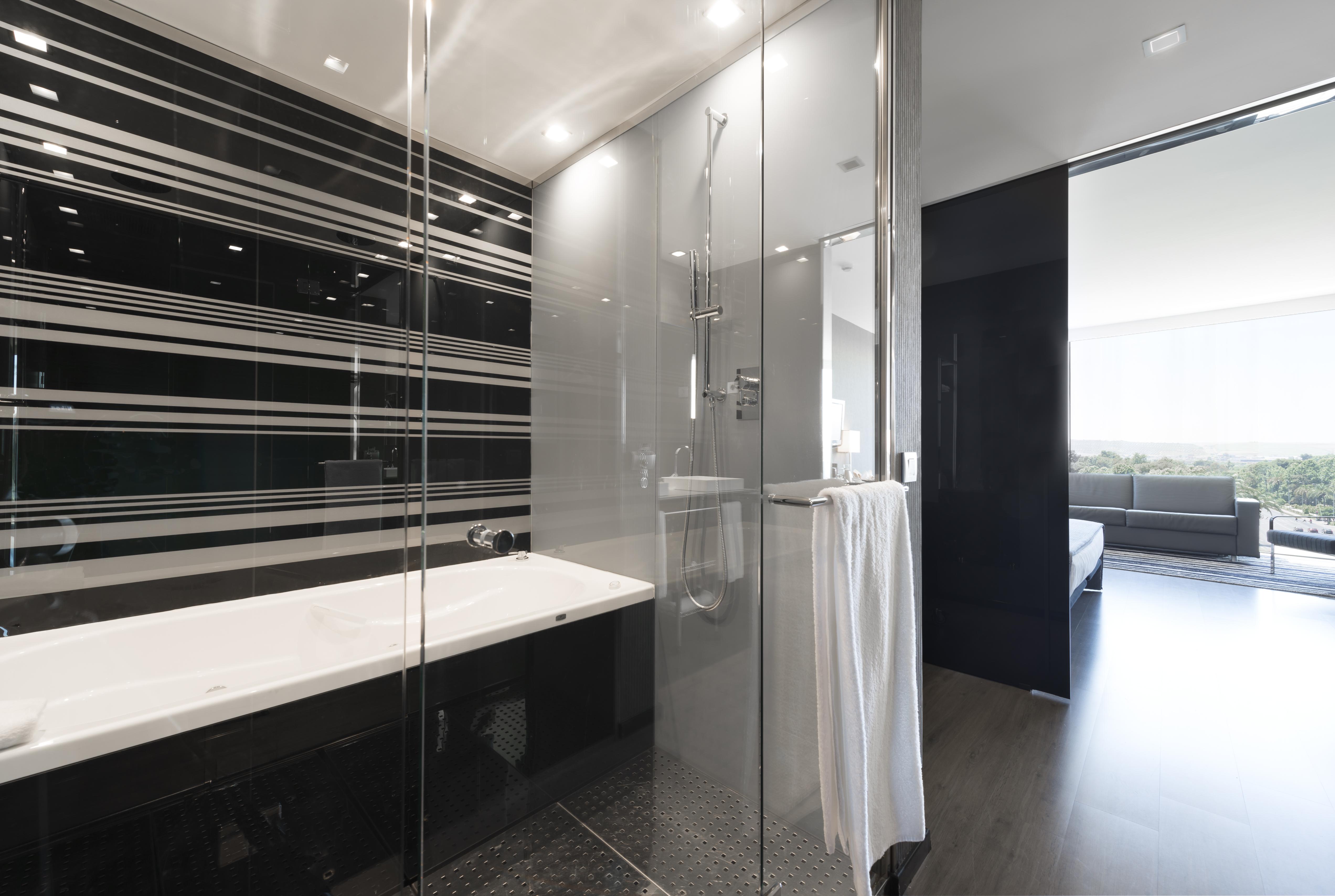 Eurostars Palace Kordoba Bagian luar foto The photo shows a modern bathroom featuring a sleek design. On one side, there is a glass-enclosed shower with contemporary fixtures. Adjacent to it, there's a stylish bathtub with a clean, white surface. The walls are decorated with a striking patte