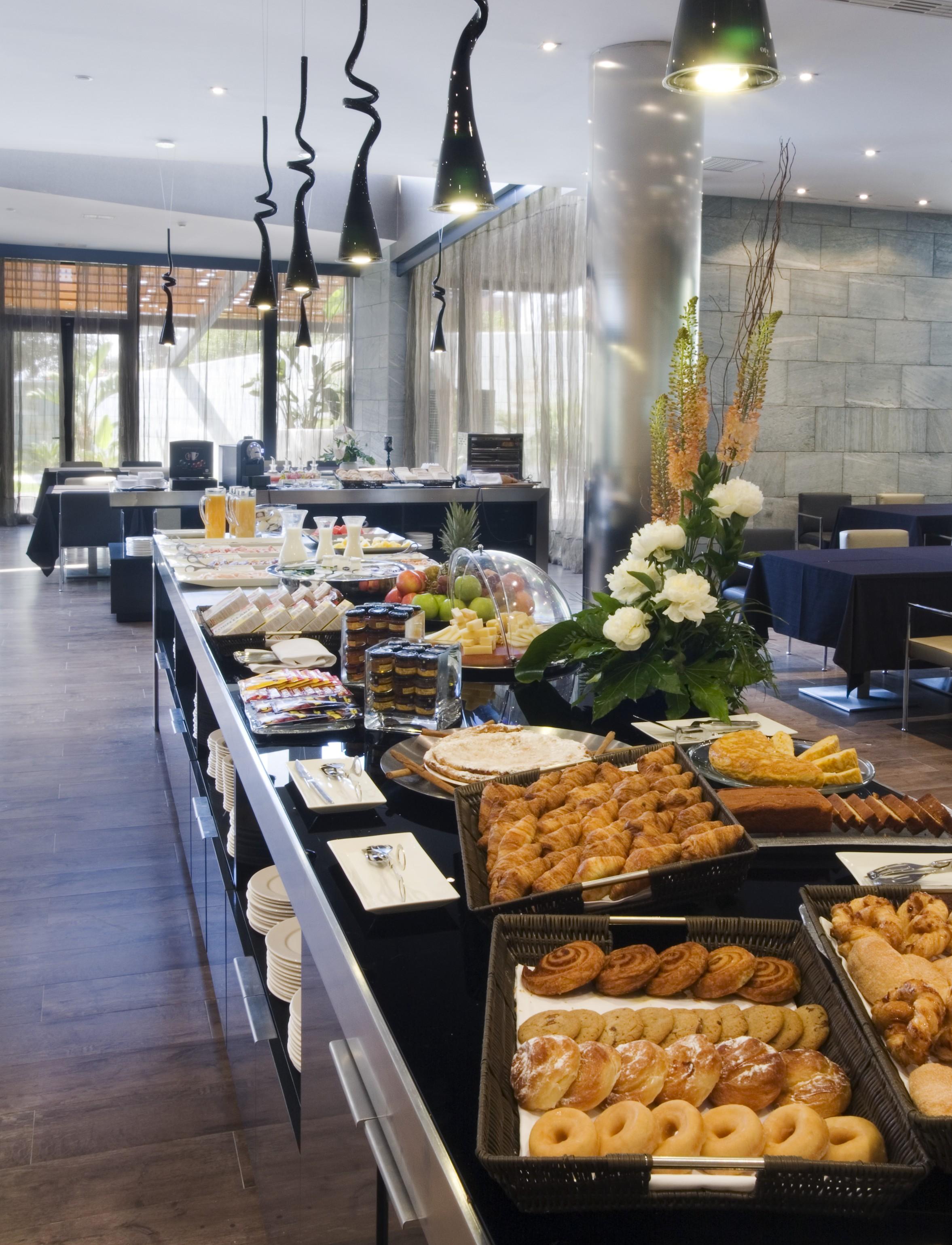 Eurostars Palace Kordoba Bagian luar foto The photo shows a beautifully arranged buffet spread in a modern setting. There are various dishes displayed on a long table, including pastries, desserts, fruits, and baked goods. A decorative arrangement of flowers enhances the presentation. The ba