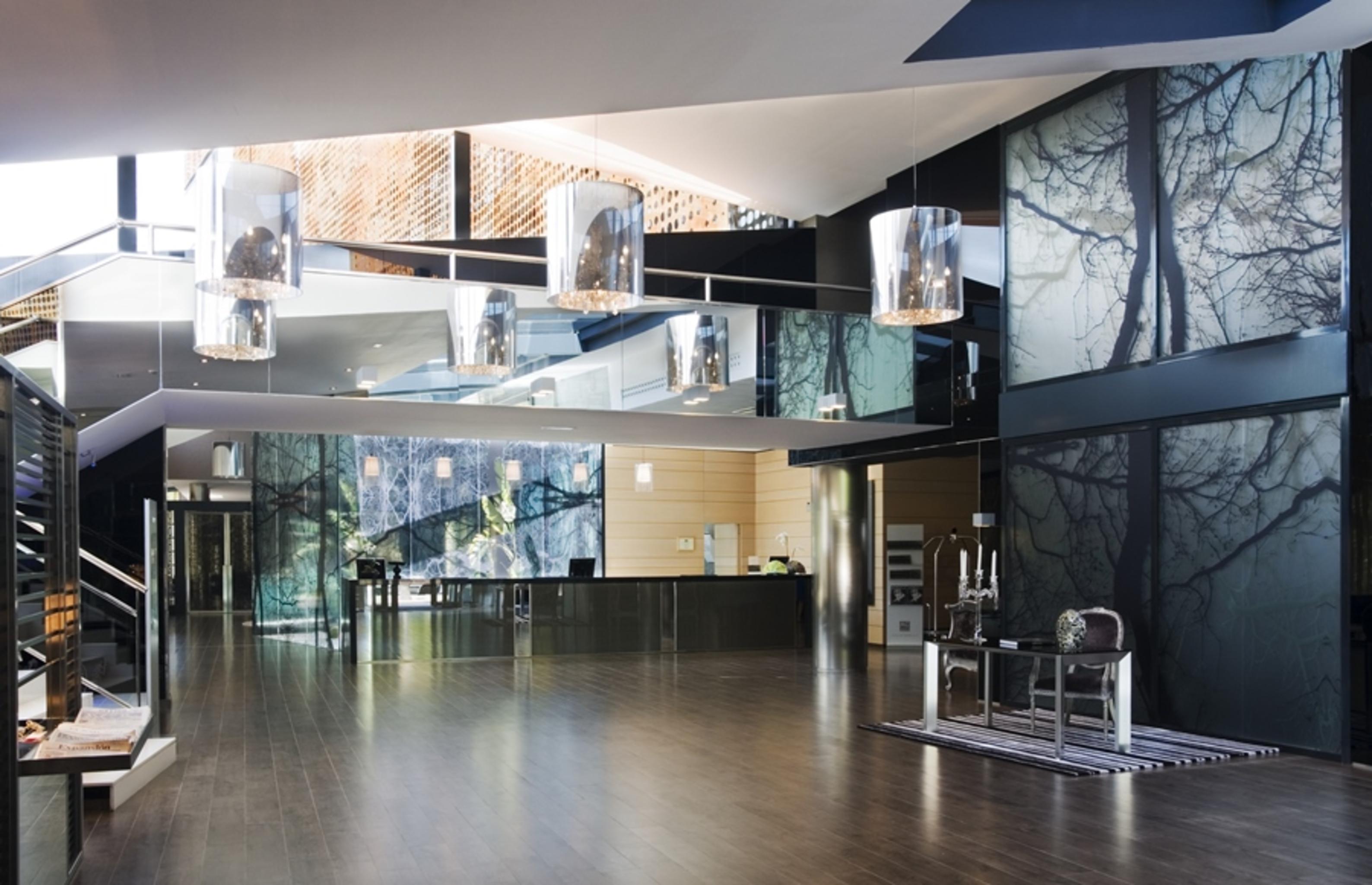 Eurostars Palace Kordoba Interior foto The photo shows a modern interior space, likely an entrance or lobby area. The design features:

- A spacious layout with a polished wooden floor.
- Large glass panels that reflect light, creating an open and airy feel.
- Artistic wall décor that inc