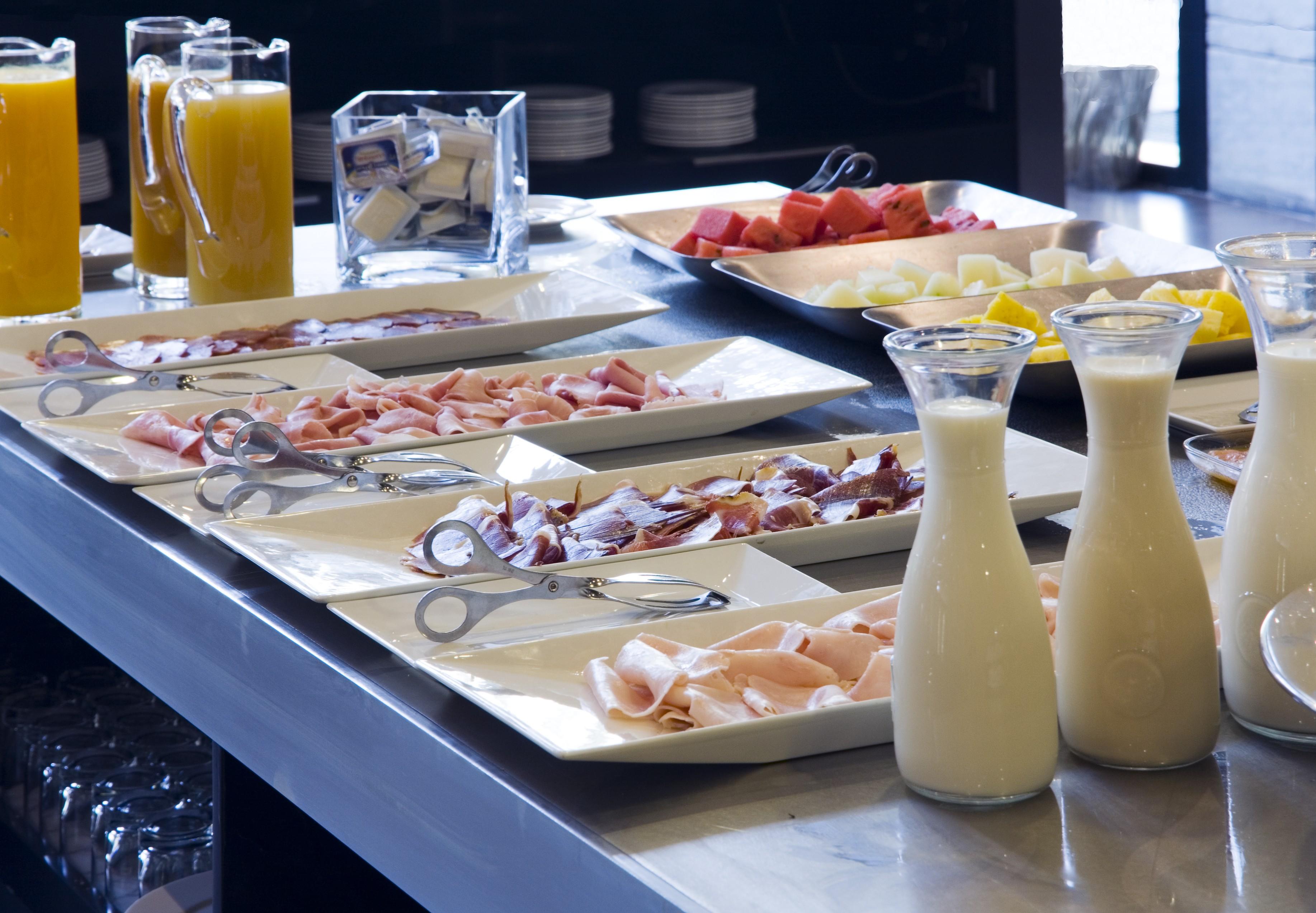 Eurostars Palace Kordoba Bagian luar foto The photo displays a buffet area with various food items arranged on a countertop. There are multiple plates featuring an assortment of sliced meats, likely including ham and possibly turkey or chicken. Additionally, two glass pitchers are filled wit