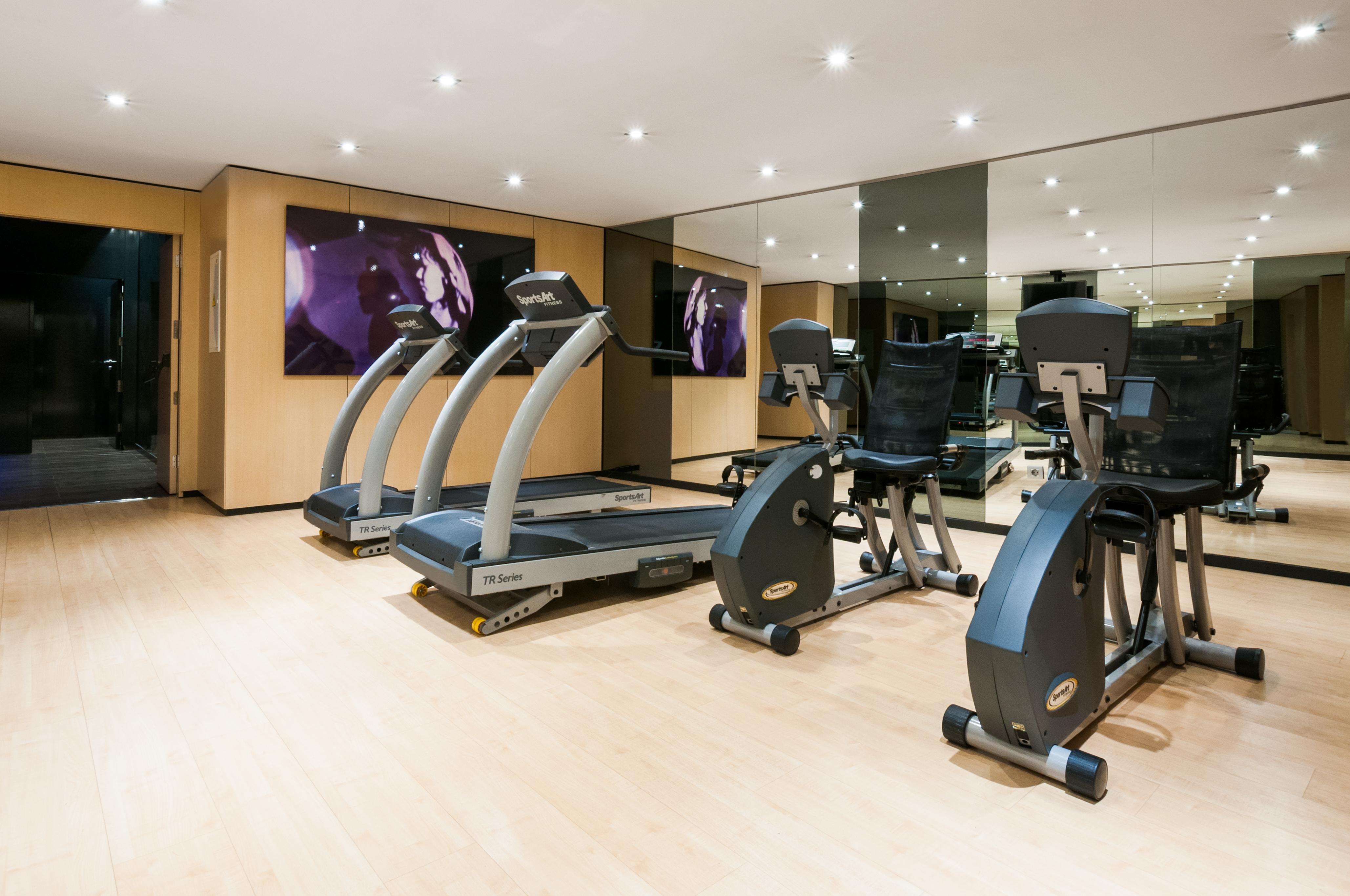 Eurostars Palace Kordoba Bagian luar foto The photo shows a modern gym or fitness area. It features several pieces of exercise equipment, including treadmills and stationary bikes. The room has bright lighting and a wooden floor, contributing to a clean and open atmosphere. There is a large 