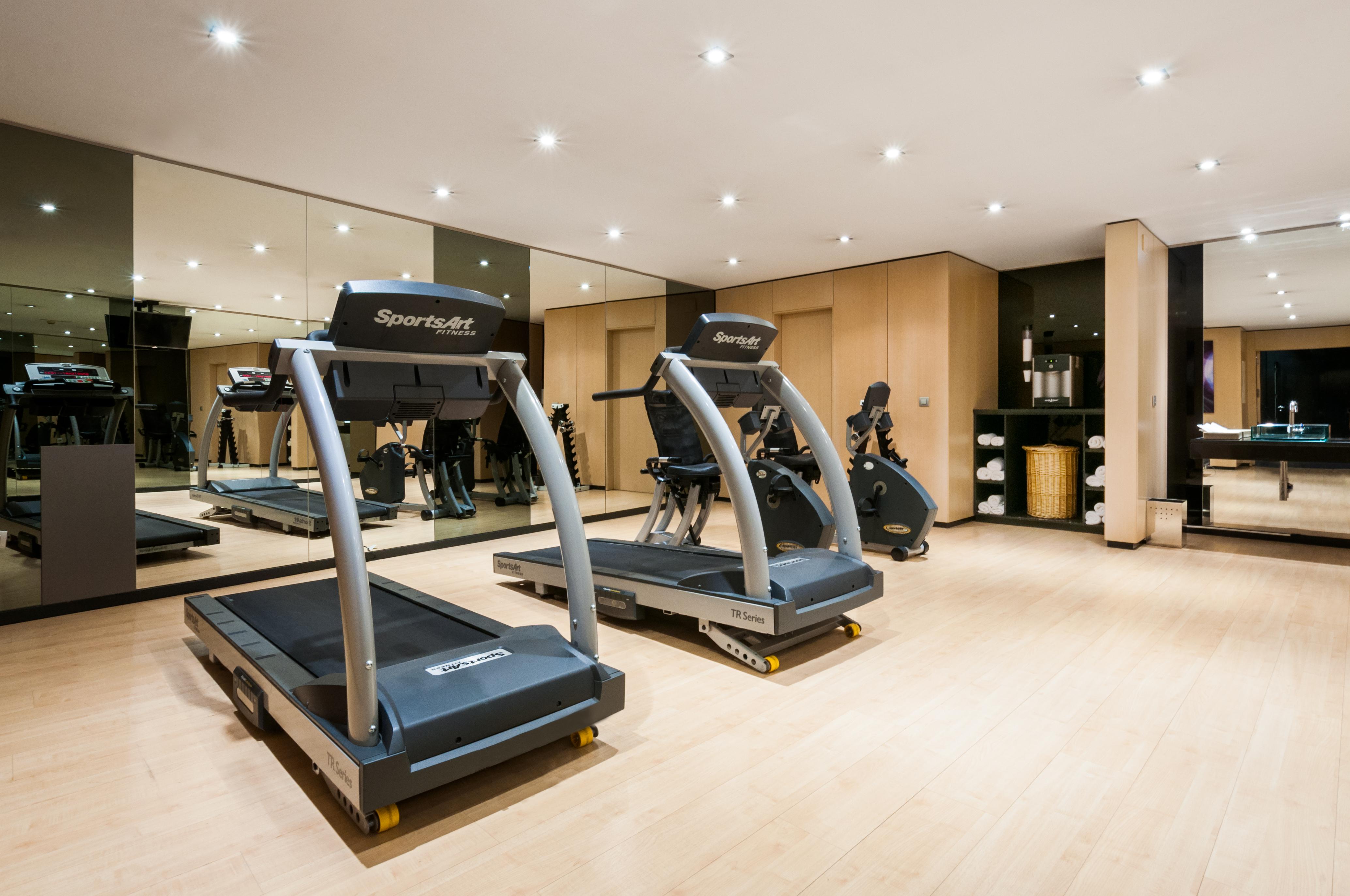 Eurostars Palace Kordoba Bagian luar foto The photo shows a modern gym or fitness area featuring two treadmills. The equipment is well-maintained and positioned on a light wooden floor. There are mirrors on the wall reflecting the workout area, which adds to the spacious feel. The overall se