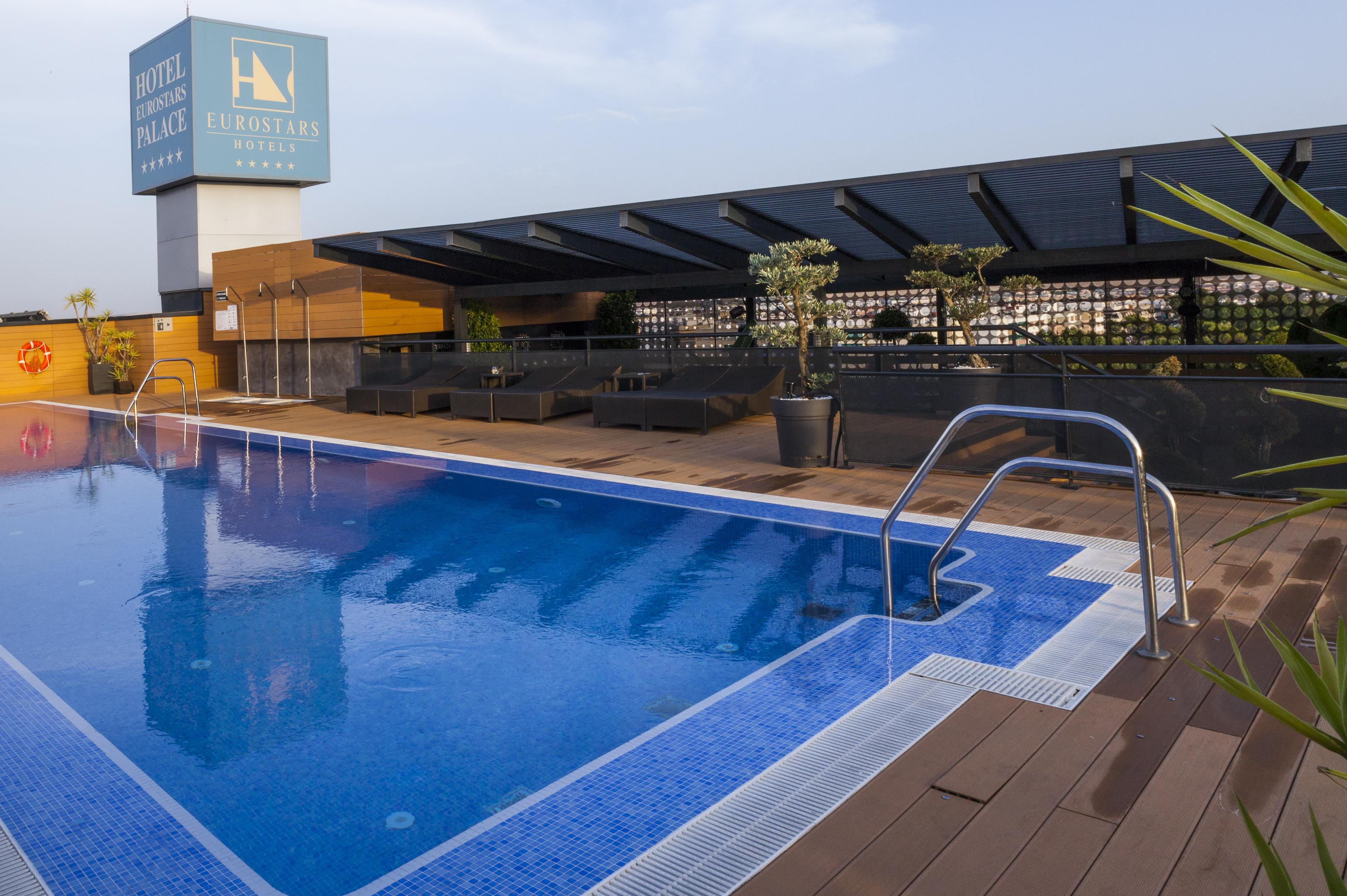 Eurostars Palace Kordoba Bagian luar foto The photo shows a rooftop swimming pool with a clear blue water surface. There is a section of the pool with a ladder for entry, and the surrounding area includes wooden decking. In the background, there is a sign for a hotel, which appears to be nam