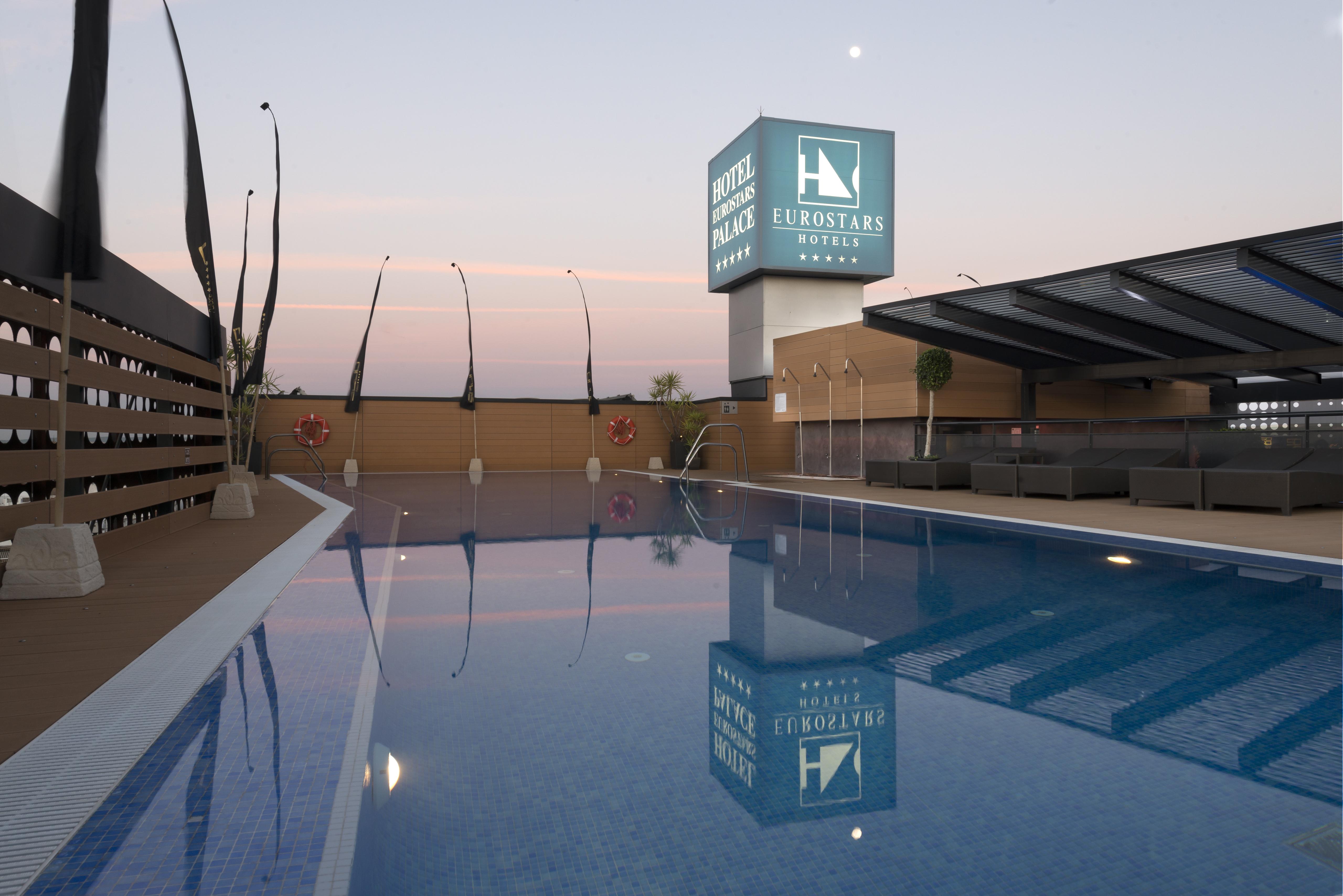 Eurostars Palace Kordoba Bagian luar foto The photo shows a rooftop space featuring a swimming pool. The pool has a clear blue water, and the area around it is designed with modern aesthetics, including a wooden deck and comfortable seating. In the background, there is a prominent sign for "