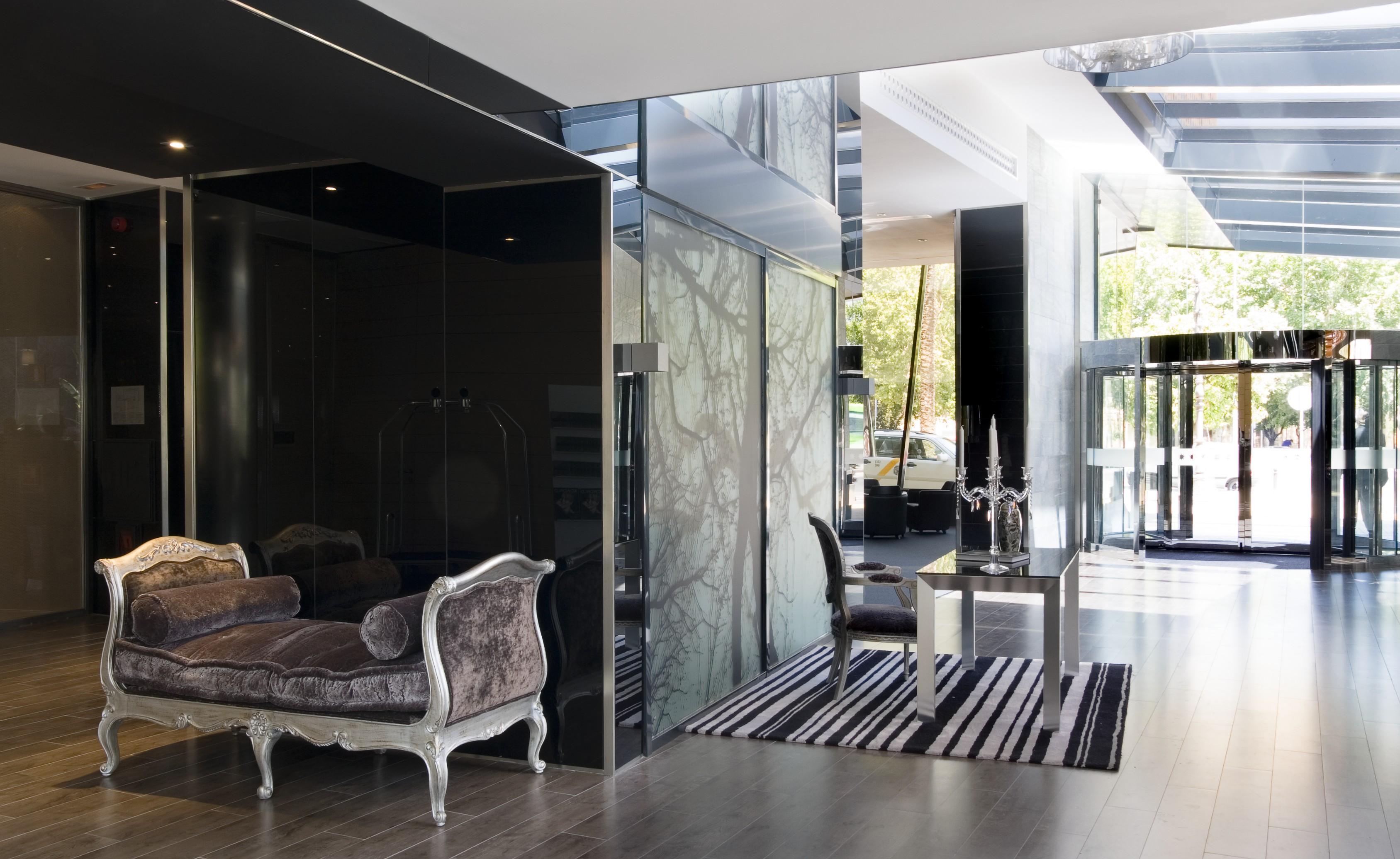 Eurostars Palace Kordoba Bagian luar foto The photo features a modern and stylish interior space, likely a lobby or reception area. On the left, there is an elegant couch with ornate detailing, set against dark, reflective walls. The floor is wooden and has a sleek design. To the right, ther