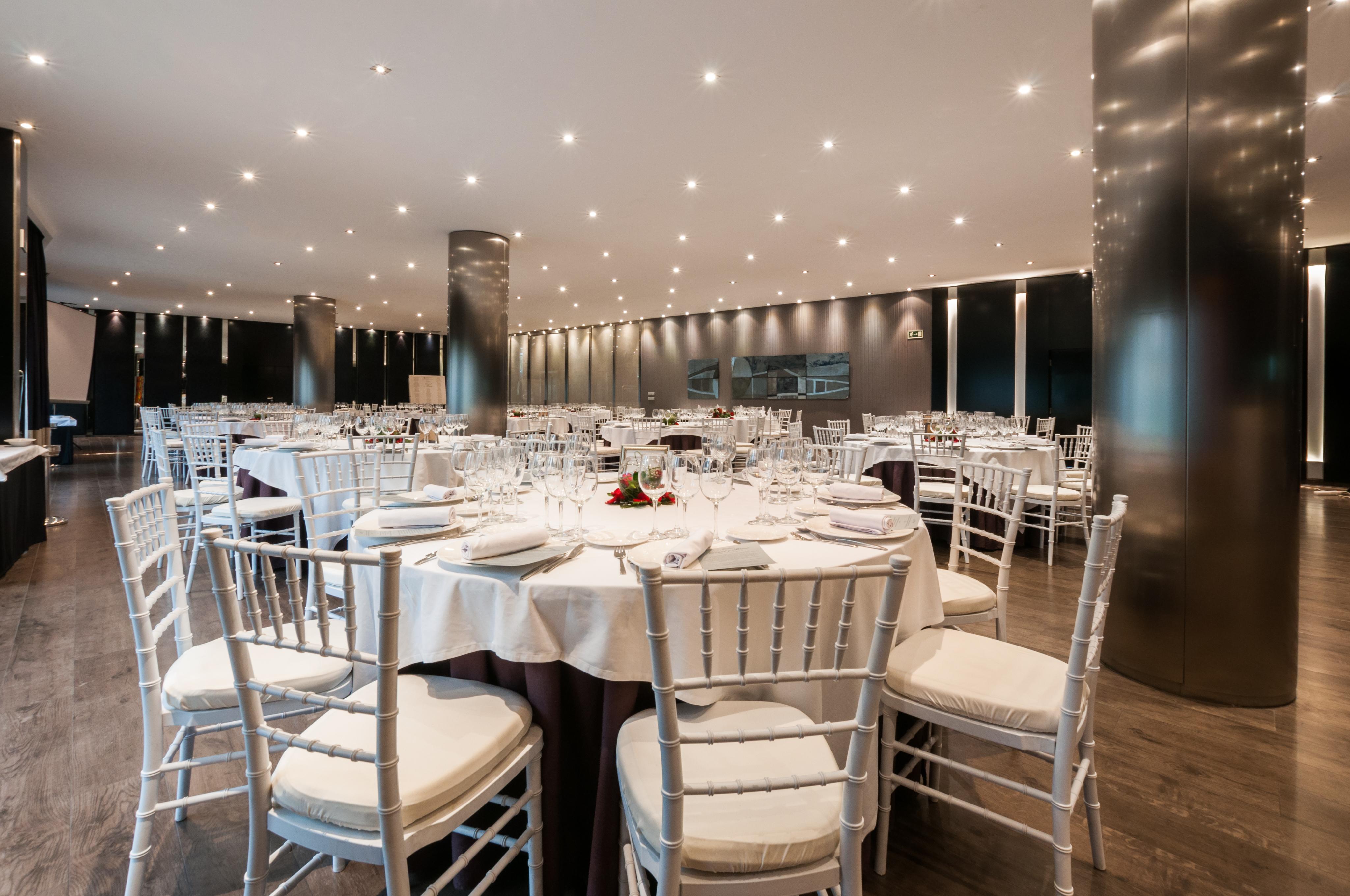 Eurostars Palace Kordoba Bagian luar foto The photo shows an elegant dining setting in a spacious restaurant. There are several round tables, each with white tablecloths and neatly arranged place settings, including glasses, plates, and utensils. The chairs are white with padded seats, provi