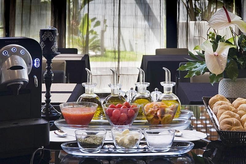 Eurostars Palace Kordoba Bagian luar foto The photo displays a stylish breakfast or brunch spread on a table. In the foreground, several small glass containers hold various ingredients: there are glasses filled with different types of oil, a bowl of fresh red tomatoes, a bowl of mixed fruit,
