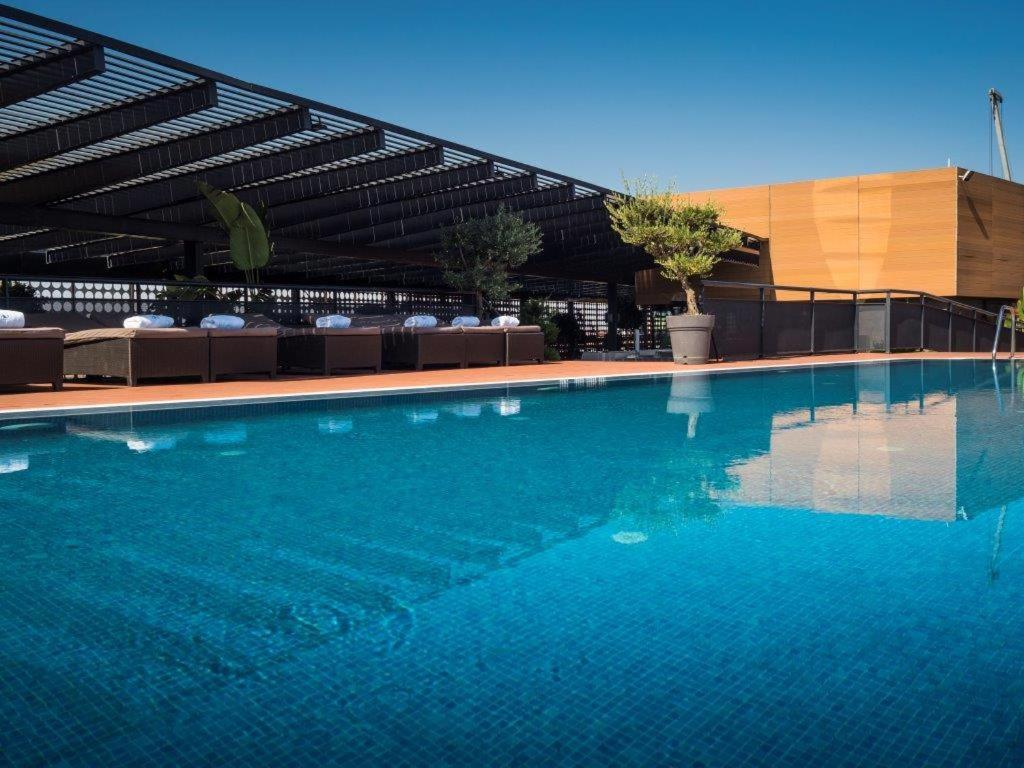 Eurostars Palace Kordoba Bagian luar foto The photo shows a rooftop swimming pool with a clear, vibrant blue surface reflecting the sky. Surrounding the pool are comfortable lounge chairs, some shaded by a modern overhead structure. The area is accented with potted plants, adding greenery to