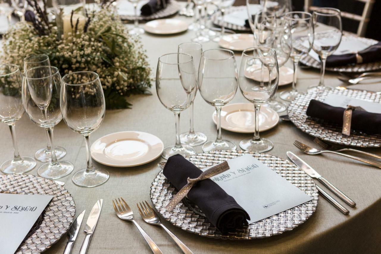Eurostars Palace Kordoba Bagian luar foto The photo shows a beautifully arranged dining table set for an event. The table has a neutral-colored tablecloth and is adorned with elegant place settings. Each setting features a decorative plate with a textured silver charger underneath, and a fol